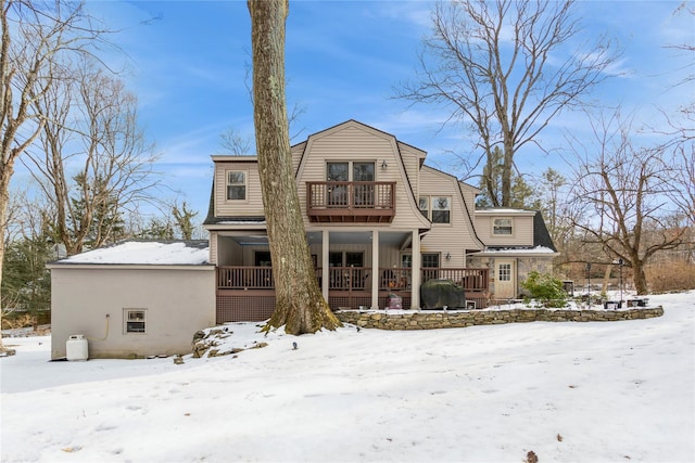 snow covered back of property with a balcony and a porch