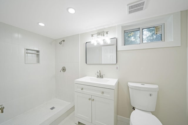 bathroom with toilet, a tile shower, and vanity