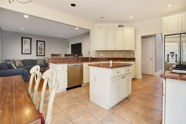 kitchen with a center island, stainless steel appliances, dark stone countertops, tasteful backsplash, and light tile patterned flooring