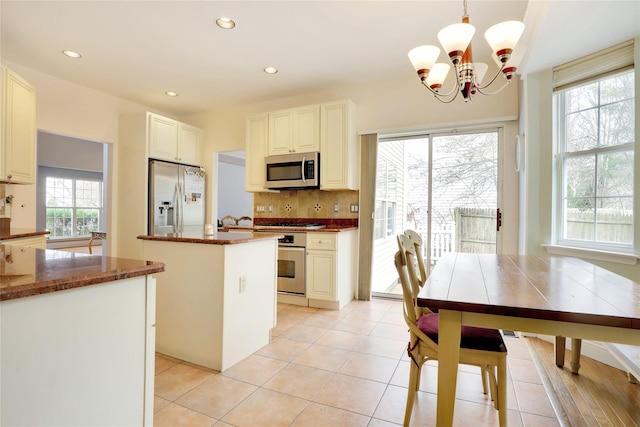 kitchen featuring appliances with stainless steel finishes, a kitchen island, white cabinetry, hanging light fixtures, and a notable chandelier