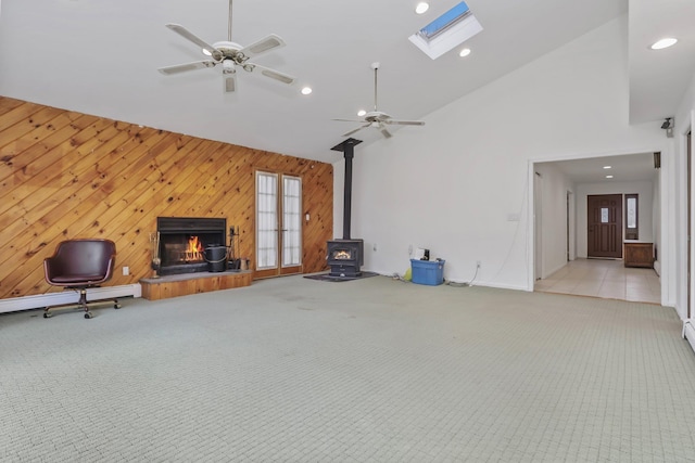 unfurnished living room featuring high vaulted ceiling, a wood stove, wooden walls, ceiling fan, and a fireplace