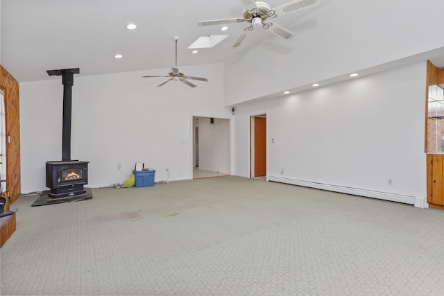 unfurnished living room featuring a skylight, a wood stove, carpet, a baseboard heating unit, and ceiling fan