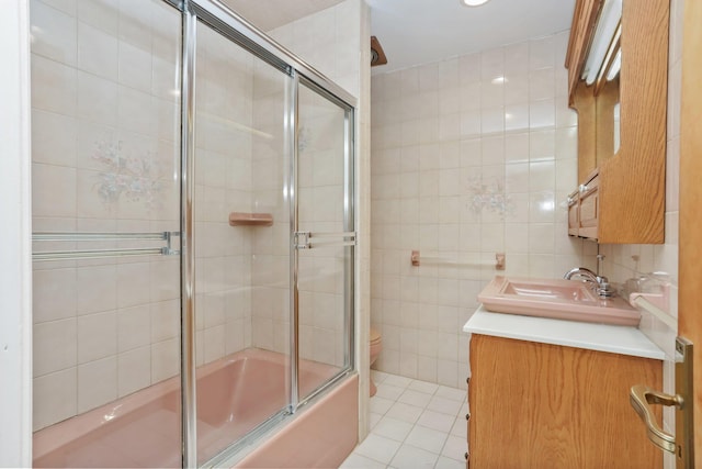 full bathroom with bath / shower combo with glass door, tile walls, tile patterned flooring, vanity, and toilet