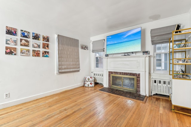 unfurnished living room with radiator, a brick fireplace, a healthy amount of sunlight, and light hardwood / wood-style floors