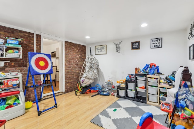 rec room featuring brick wall and hardwood / wood-style floors