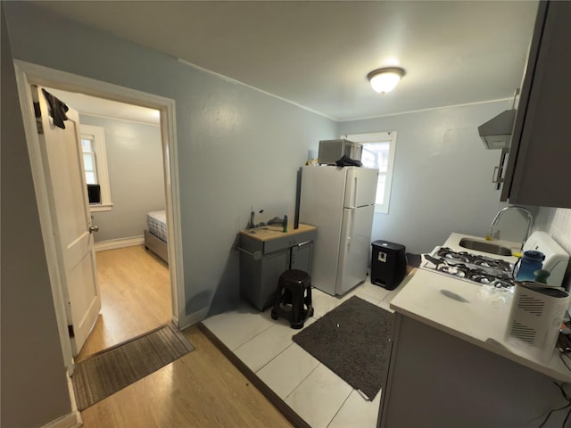 kitchen with white refrigerator, ventilation hood, sink, and light hardwood / wood-style flooring