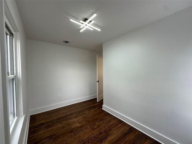 unfurnished room with dark wood-style flooring, visible vents, and baseboards