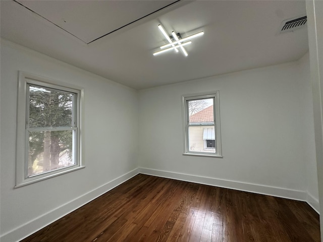 unfurnished room featuring dark wood-type flooring, attic access, visible vents, and baseboards