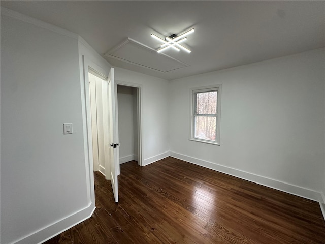 unfurnished room featuring dark wood-style flooring, attic access, and baseboards