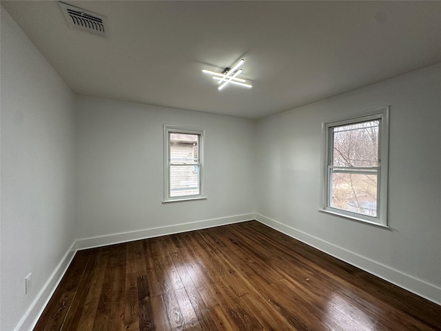 spare room featuring dark wood-style floors, visible vents, and baseboards