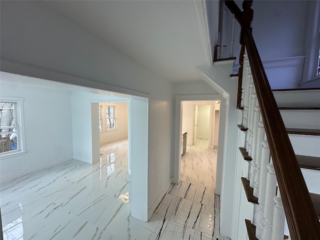 hallway featuring lofted ceiling, marble finish floor, stairs, and baseboards