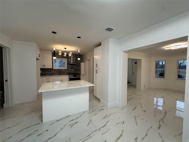 kitchen with marble finish floor, wall chimney exhaust hood, white cabinetry, and decorative backsplash