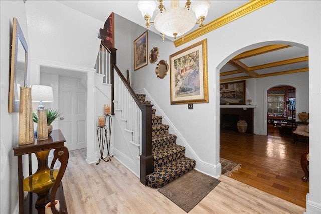 entrance foyer with coffered ceiling, a notable chandelier, beamed ceiling, and light wood-type flooring