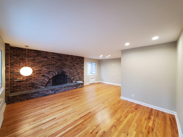 unfurnished living room with radiator, a brick fireplace, and light hardwood / wood-style floors