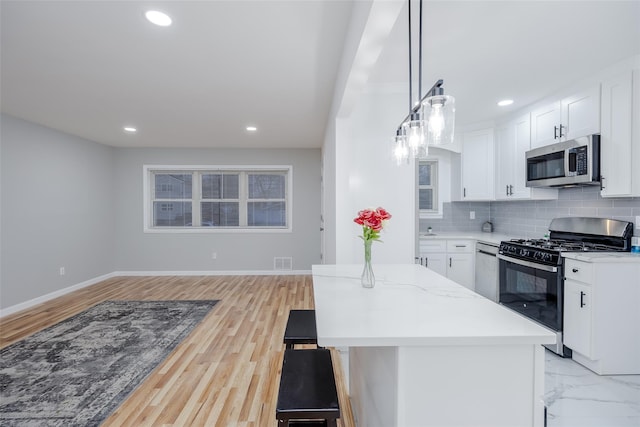 kitchen with appliances with stainless steel finishes, decorative backsplash, decorative light fixtures, light stone countertops, and white cabinets