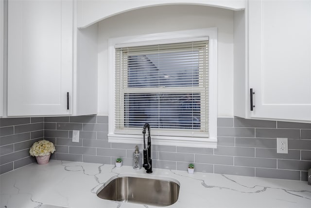 details featuring decorative backsplash, sink, light stone counters, and white cabinetry