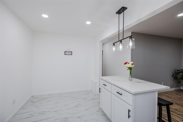 interior space with decorative light fixtures, kitchen peninsula, white cabinetry, light stone countertops, and a kitchen breakfast bar