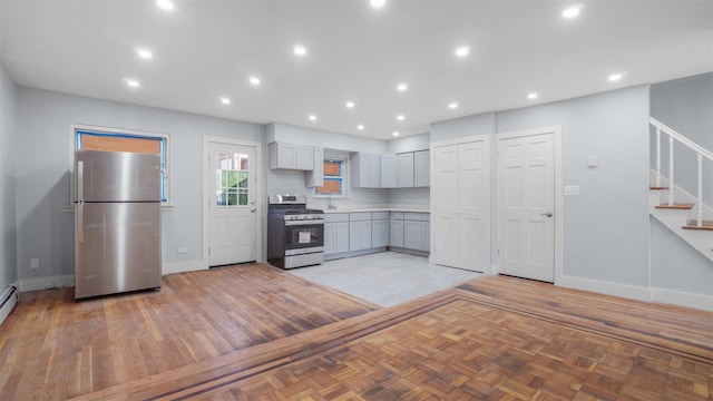 kitchen with light parquet flooring, gray cabinetry, stainless steel appliances, and a baseboard radiator