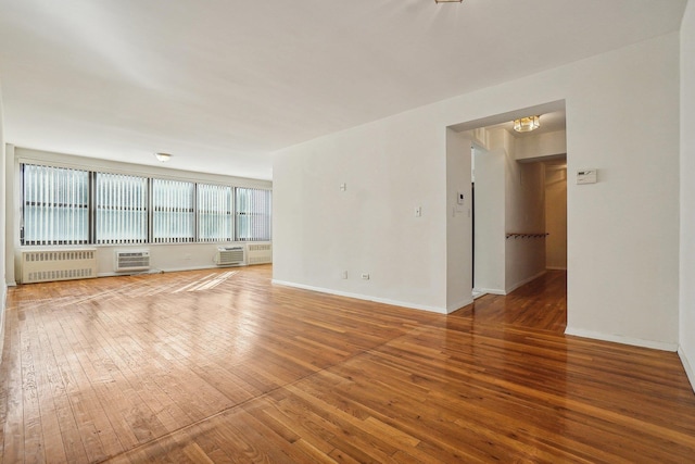 unfurnished living room with wood-type flooring, an AC wall unit, and radiator heating unit