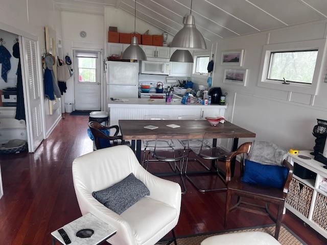 kitchen with pendant lighting, dark wood-type flooring, white appliances, and lofted ceiling