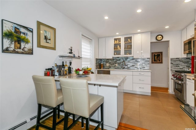 kitchen featuring white cabinetry, kitchen peninsula, a breakfast bar area, appliances with stainless steel finishes, and decorative backsplash