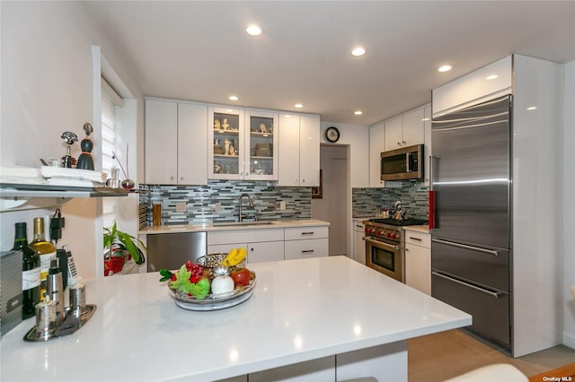 kitchen with white cabinetry, decorative backsplash, premium appliances, and sink