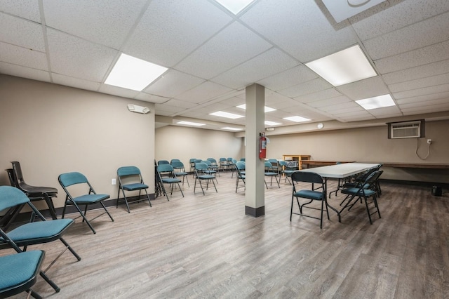 interior space with an AC wall unit, a drop ceiling, and wood-type flooring