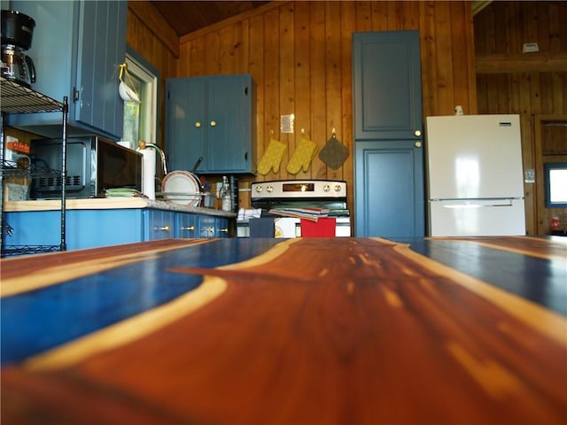 kitchen with electric range, vaulted ceiling, white refrigerator, and wooden walls