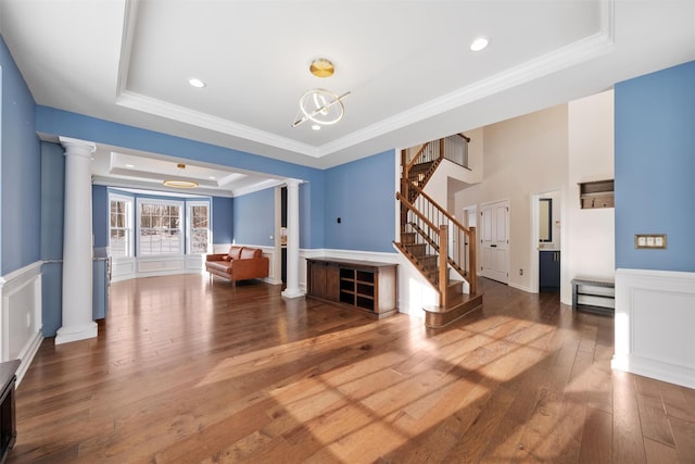 interior space featuring a raised ceiling, hardwood / wood-style floors, ornamental molding, and ornate columns