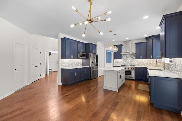 kitchen featuring appliances with stainless steel finishes, a center island, wall chimney exhaust hood, sink, and hanging light fixtures