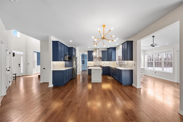 kitchen with tasteful backsplash, sink, appliances with stainless steel finishes, blue cabinets, and wall chimney exhaust hood