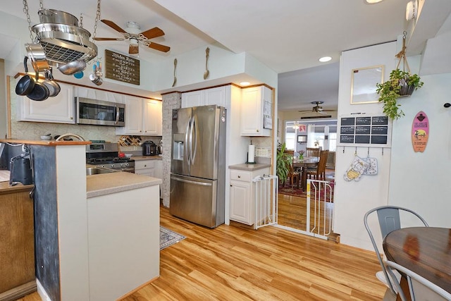 kitchen featuring white cabinets, decorative backsplash, ceiling fan, stainless steel appliances, and light wood-type flooring