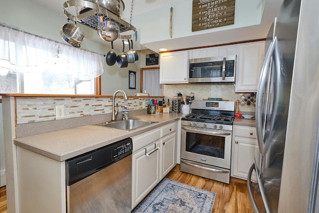 kitchen with sink, appliances with stainless steel finishes, white cabinetry, tasteful backsplash, and light wood-type flooring