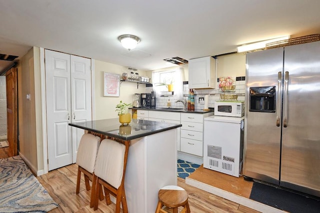 kitchen with sink, white cabinetry, a center island, stainless steel refrigerator with ice dispenser, and light wood-type flooring