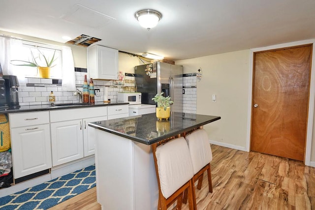 kitchen with sink, white cabinetry, stainless steel refrigerator with ice dispenser, a kitchen island, and decorative backsplash