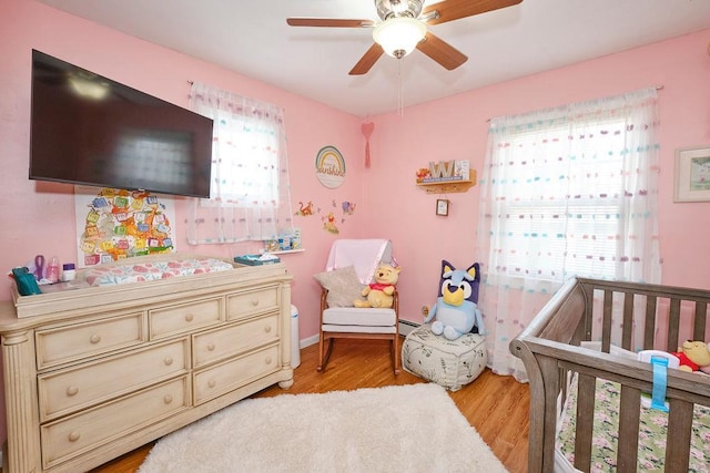 bedroom featuring a crib, ceiling fan, light wood-type flooring, and multiple windows