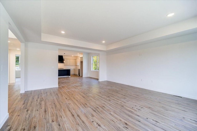 unfurnished living room featuring light wood-type flooring and a tray ceiling