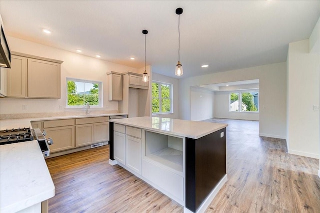 kitchen featuring pendant lighting, stainless steel range oven, a kitchen island, sink, and light hardwood / wood-style flooring