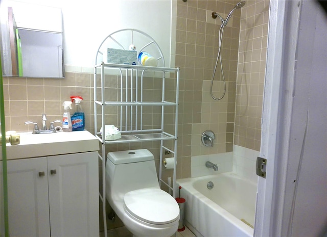 full bathroom featuring toilet, tiled shower / bath, tasteful backsplash, tile walls, and vanity