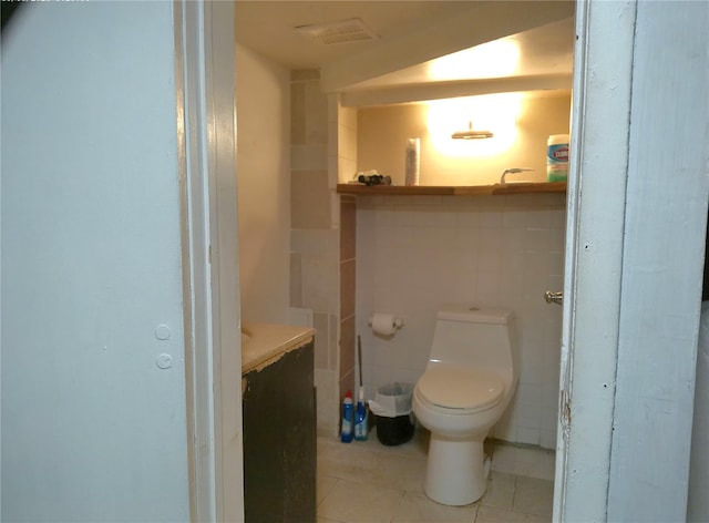 bathroom with toilet, vanity, tile walls, and tile patterned flooring