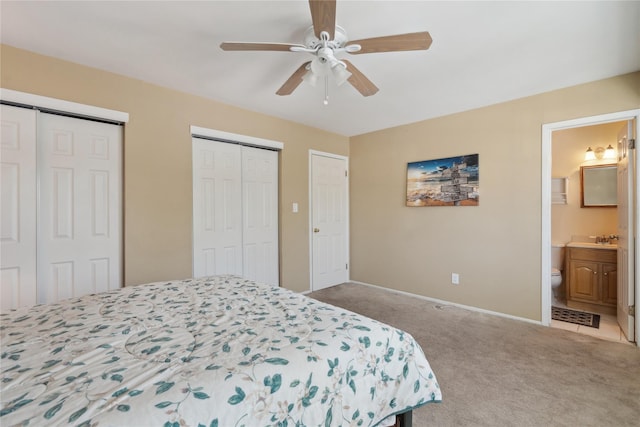 bedroom with light carpet, connected bathroom, two closets, and ceiling fan