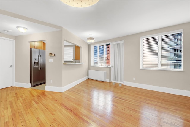 unfurnished living room featuring sink, radiator heating unit, and light hardwood / wood-style flooring