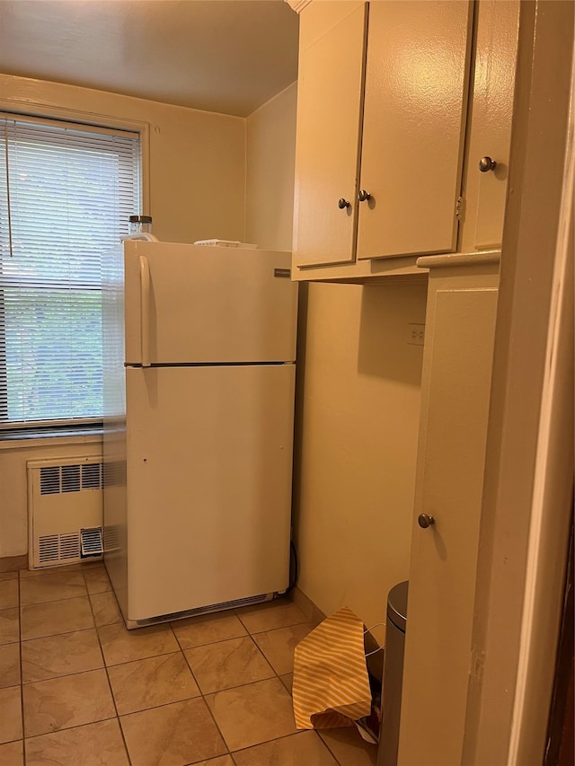 kitchen featuring light tile patterned floors, radiator heating unit, white fridge, and white cabinetry