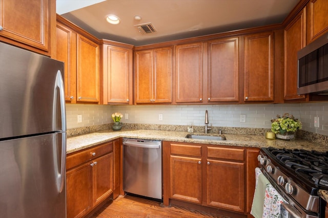 kitchen featuring appliances with stainless steel finishes, tasteful backsplash, sink, light wood-type flooring, and light stone counters