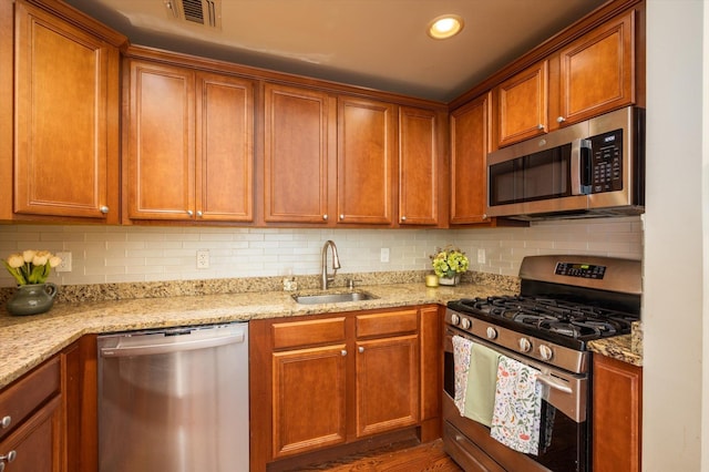 kitchen with light stone countertops, appliances with stainless steel finishes, backsplash, and sink