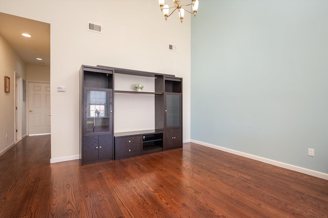 unfurnished living room featuring an inviting chandelier, dark hardwood / wood-style flooring, and a high ceiling