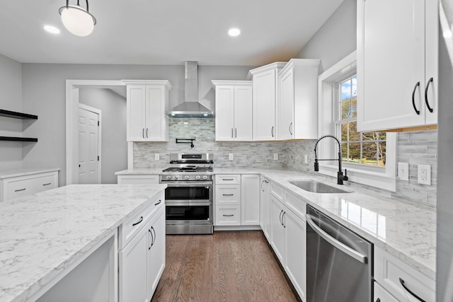 kitchen featuring dark wood-style floors, appliances with stainless steel finishes, wall chimney range hood, white cabinetry, and a sink