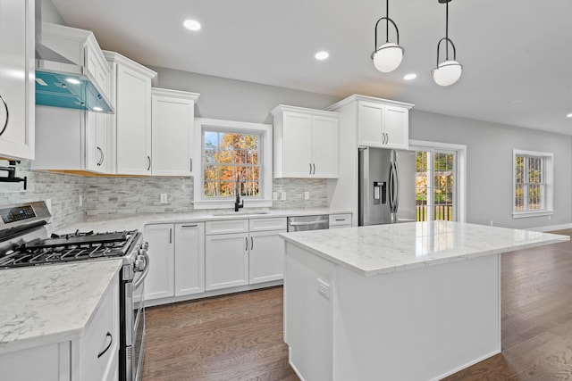 kitchen with dark wood-style floors, stainless steel appliances, wall chimney range hood, and a sink