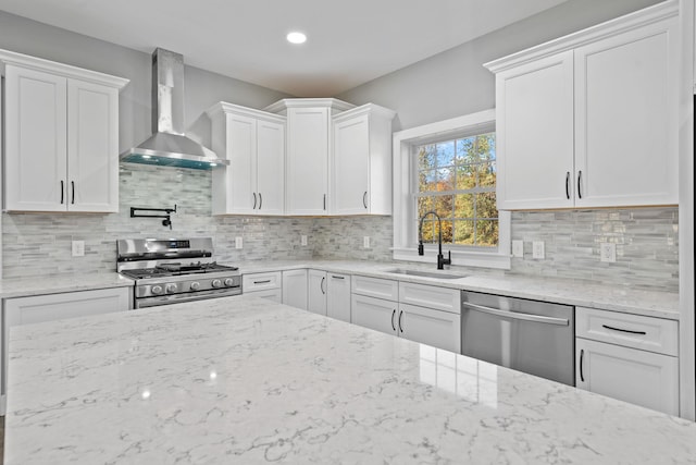 kitchen featuring wall chimney range hood, appliances with stainless steel finishes, white cabinets, and a sink