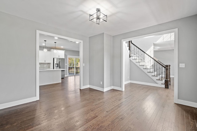 unfurnished living room with an inviting chandelier, baseboards, stairway, and dark wood finished floors